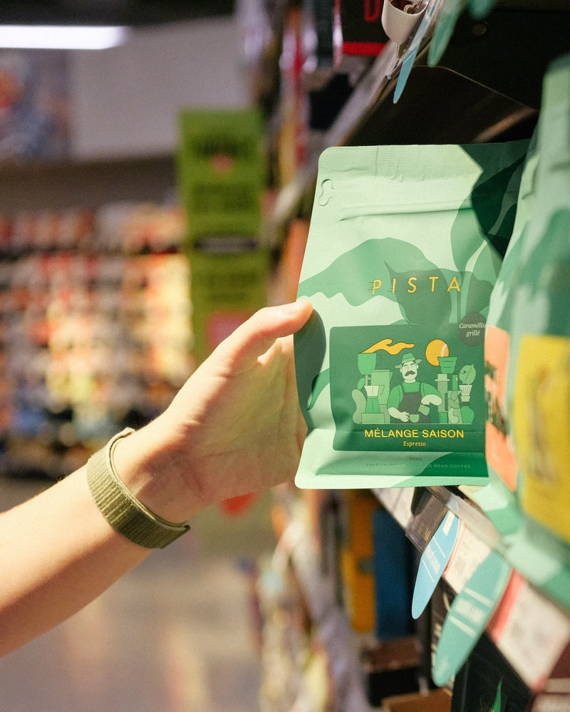 Hand holding a green bag of packaged specialty coffee in a grocery store aisle